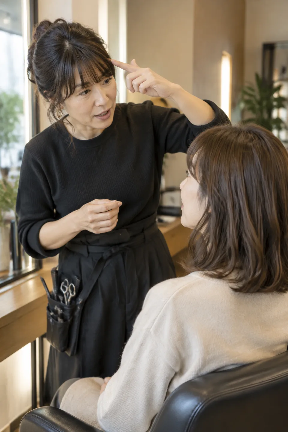 Hairstylist pointing to her fringe while discussing a hairstyle with a seated client